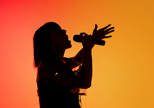 Silhouette einer Sängerin vor einem orangefarbenen Studiohintergrund